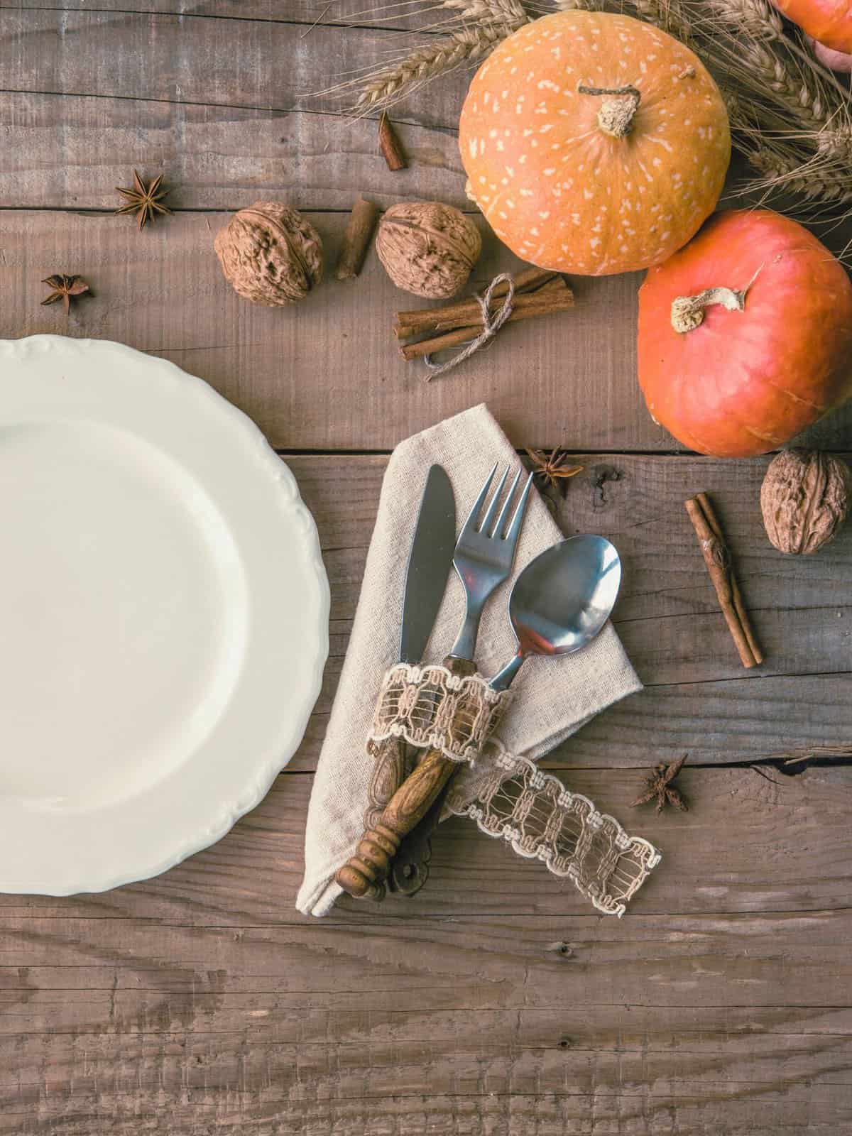 rustic place setting with white china, cutlery on linen & styled with autumn harvest vegetables, spices & nuts